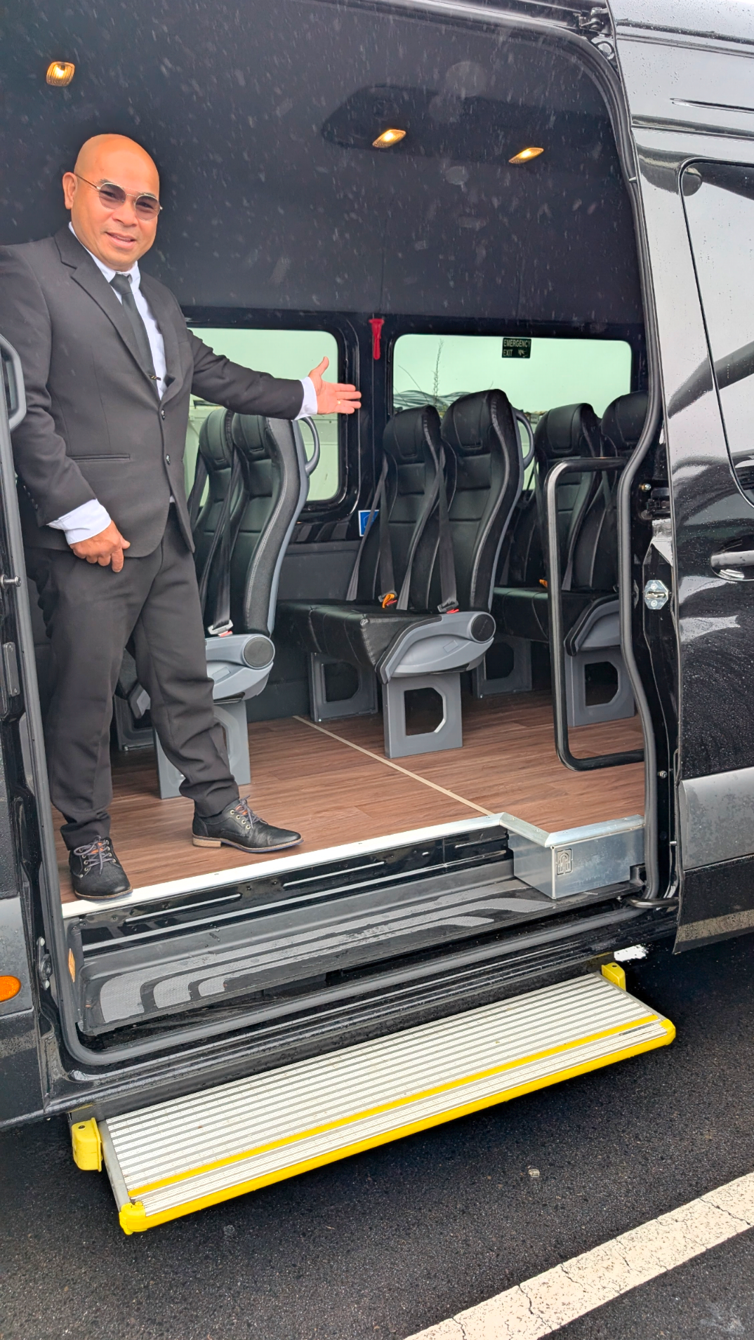 Man in suit stands inside black van.